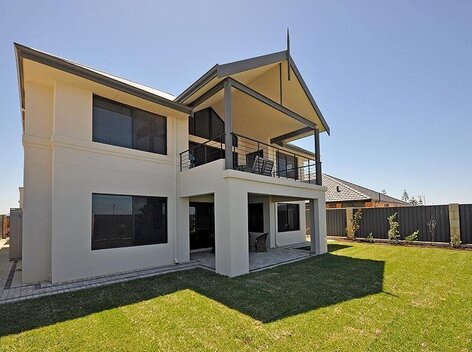 New two storey house with balcony and patio surrounded by grassy lawn